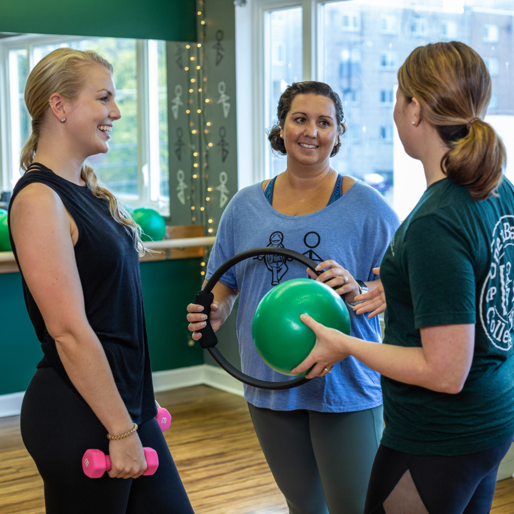 Group of three women chatting in exercise studio while holding workout equipment