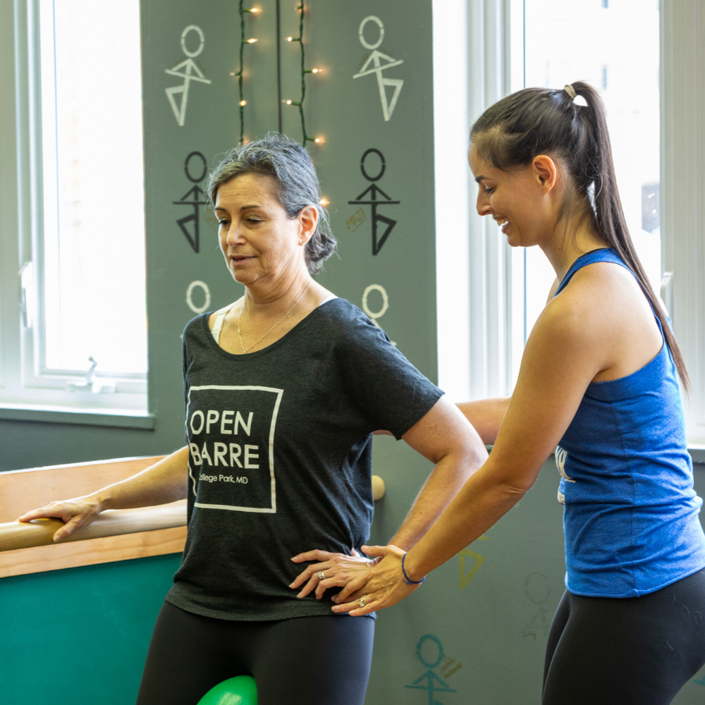 Instructor providing hands-on adjustment to woman for posture during barre fitness class