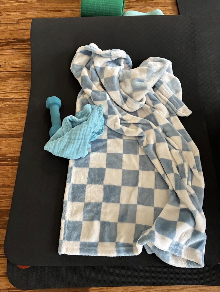Soft checkered baby blanket and muslin cloth laid out on an exercise mat beside a hand weight